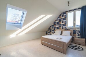 A bedroom with a sloped ceiling, a skylight, a bed, bedside tables, and a patterned wall.