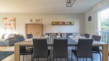 Un comedor moderno con una mesa de madera y sillas negras, una zona de cocina con armarios, y vista al exterior a través de un ventanal grande.