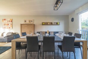 Een moderne eetruimte met een houten tafel en zwarte stoelen, een keuken met kasten, en uitzicht op het omliggende landschap door een groot raam.