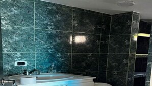 Een badkamer met een witte wastafel, een toilet en donkergroene marmeren tegels.