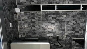 Een kleine kamer met een metallic apparaat, mogelijk een wasmachine, en een betegelde muur met een geometrisch patroon.