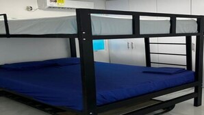 Een stapelbed met een blauwe matras in een kamer met witte wanden en een plafondlamp.
