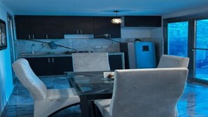 Een moderne keuken met donkere kastjes, een glazen eettafel en een blauwe koelkast.