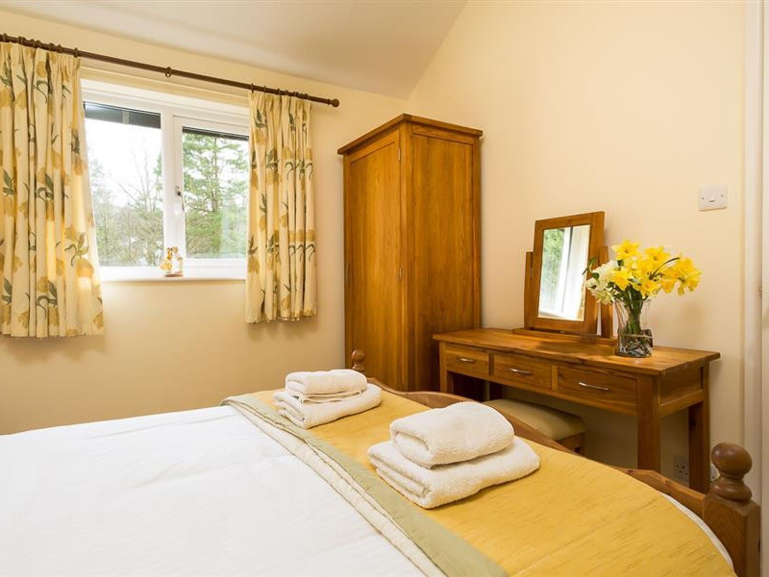 Un dormitorio con cama, cómoda de madera, espejo y ventana con cortinas.