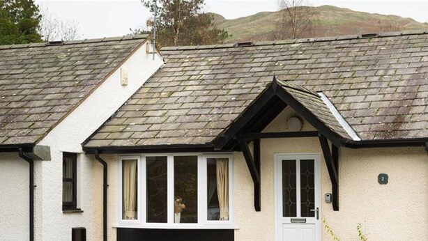 A two-story house with a white exterior, a black door, and a small porch. - 2 Riverside Cottage (Ambleside)