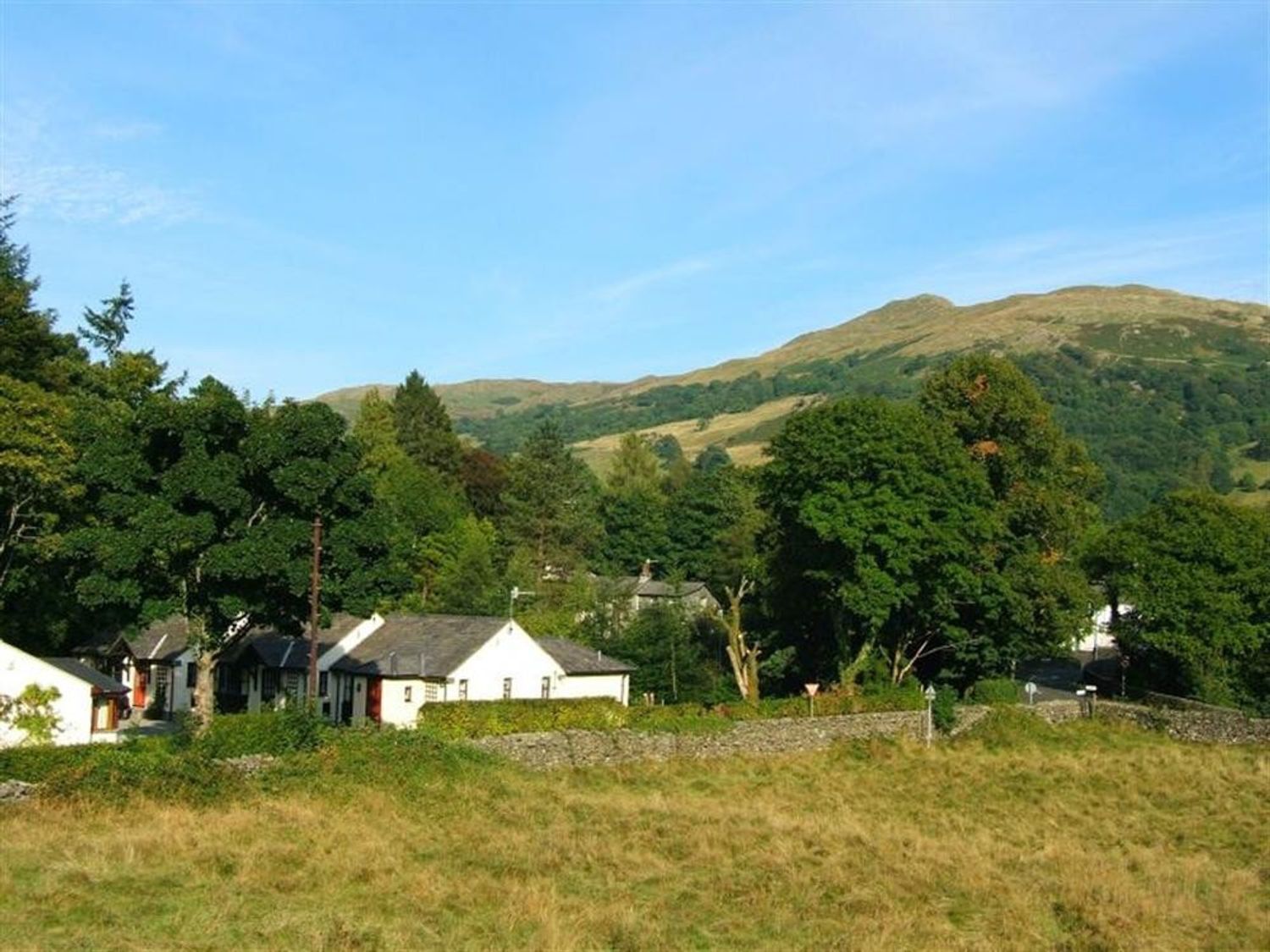 Ländliche Landschaft mit Häusern, eingebettet zwischen Bäumen und Hügeln.