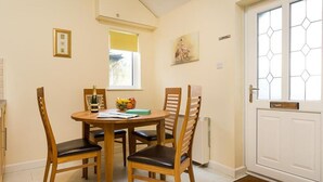 A dining area with a round table, four wooden chairs, a bottle of champagne, and a fruit bowl. - 2 Riverside Cottage (Ambleside)