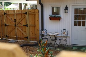 A wooden gate, a white door, a small table with chairs, and a hanging planter.