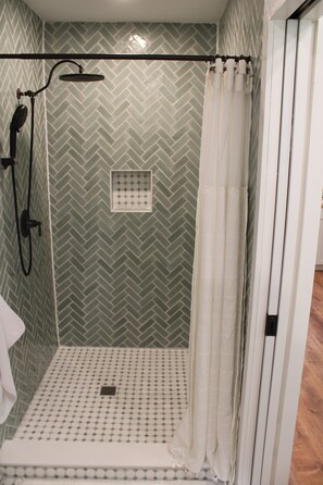 A shower area with a herringbone-patterned wall, a showerhead, and a curtain.