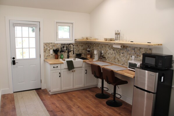 A compact kitchen with white cabinets, a wooden countertop, a stainless steel refrigerator, and a microwave.