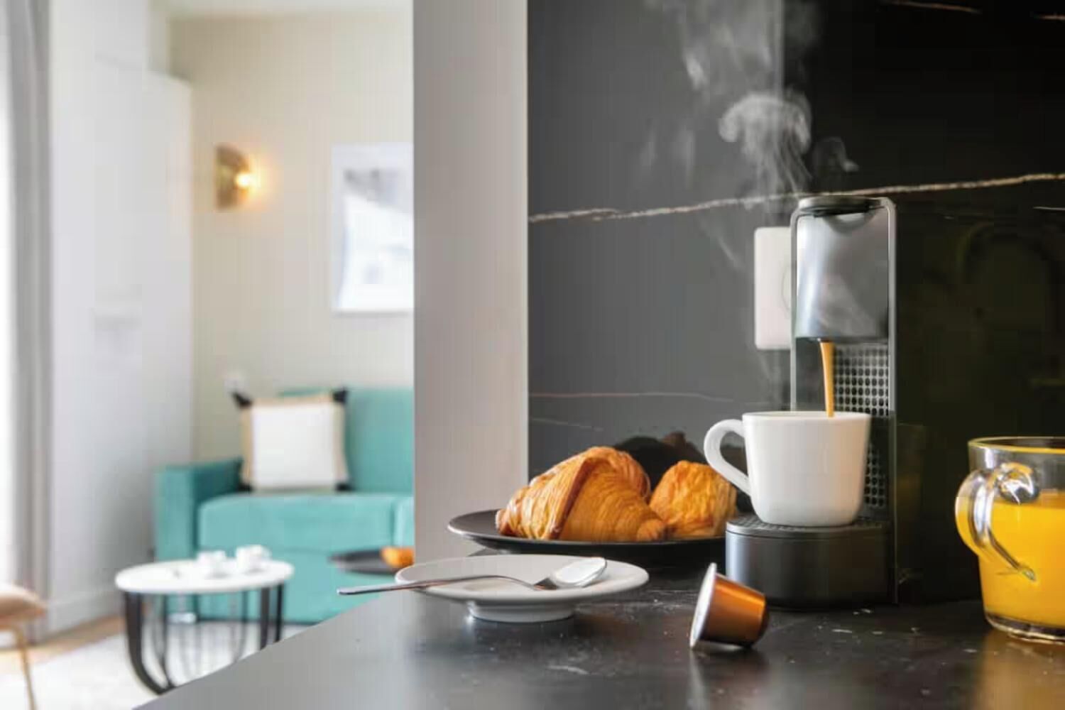 Eine moderne Küche mit Kaffeemaschine, Croissants, einer Kaffeetasse und einem Glas Orangensaft auf der Arbeitsfläche.