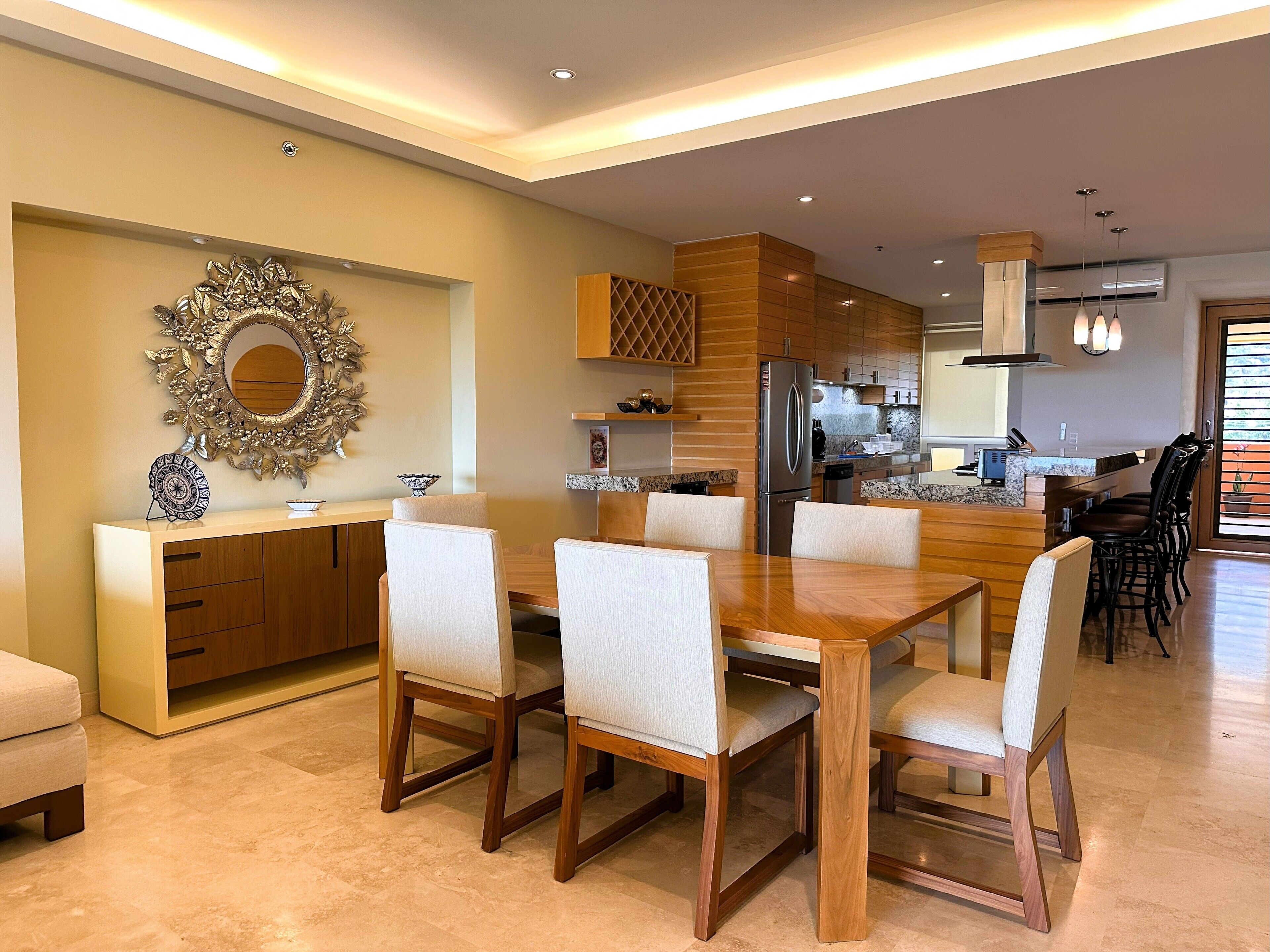 Una cocina moderna con armarios de madera, un refrigerador de acero inoxidable y un comedor con mesa y sillas de madera.