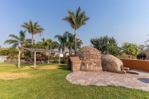 A courtyard with a stone structure, palm trees, and a pergola.