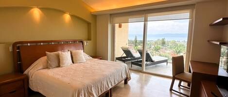 A bedroom with a large bed, a desk, and a chair, a balcony with a view.
