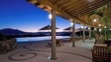 A poolside area with lounge chairs and umbrellas, a stone wall, and a view of mountains at dusk.