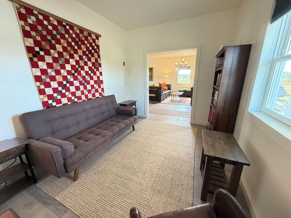 A living room with a grey sofa, a wooden coffee table, and a large red and white quilt on the wall. - Secluded blueberry field retreat with sweeping 360 views. (Cherryfield)