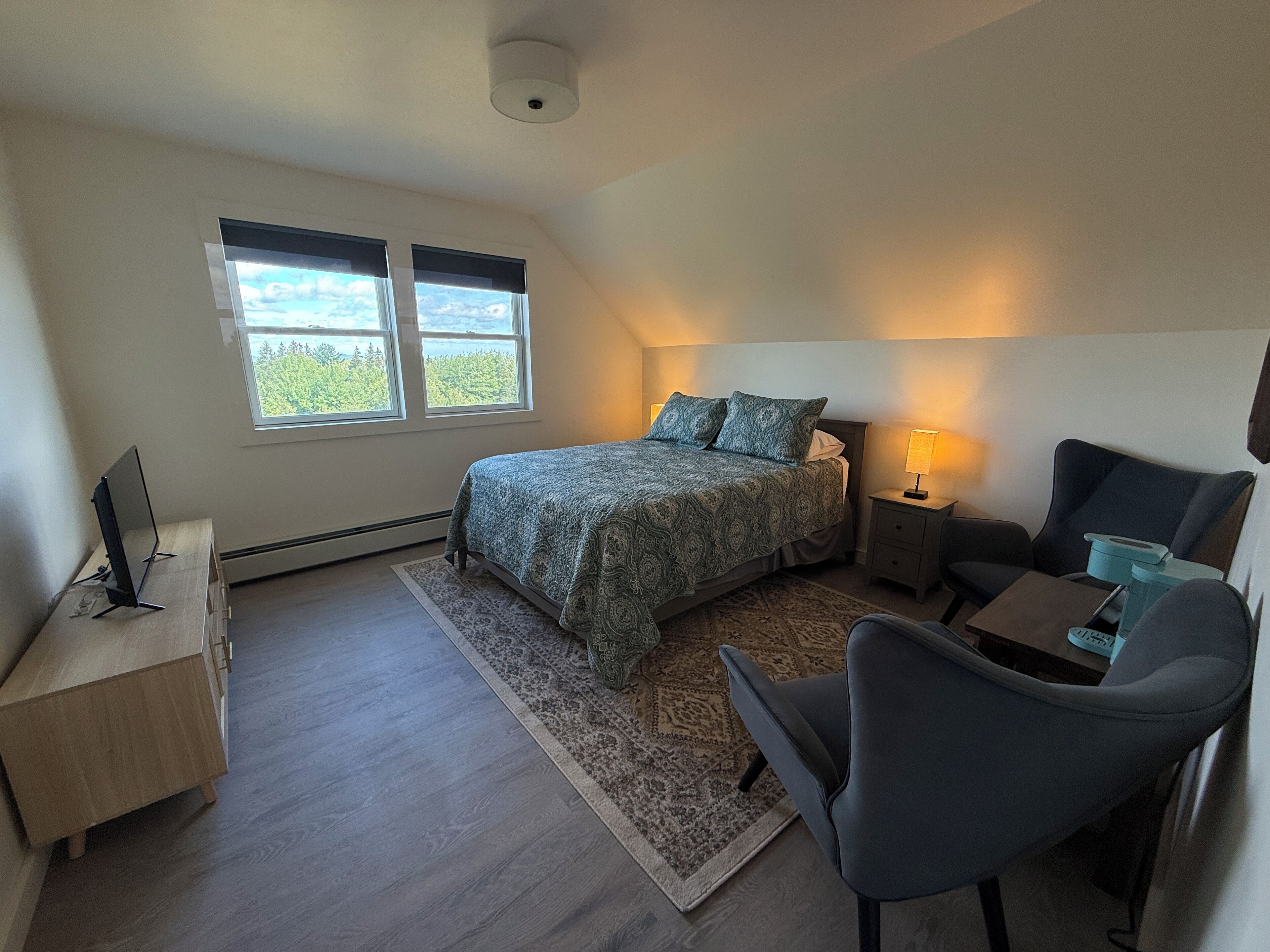 Un dormitorio con cama, mesita de noche, silla, escritorio y ventana con vistas.