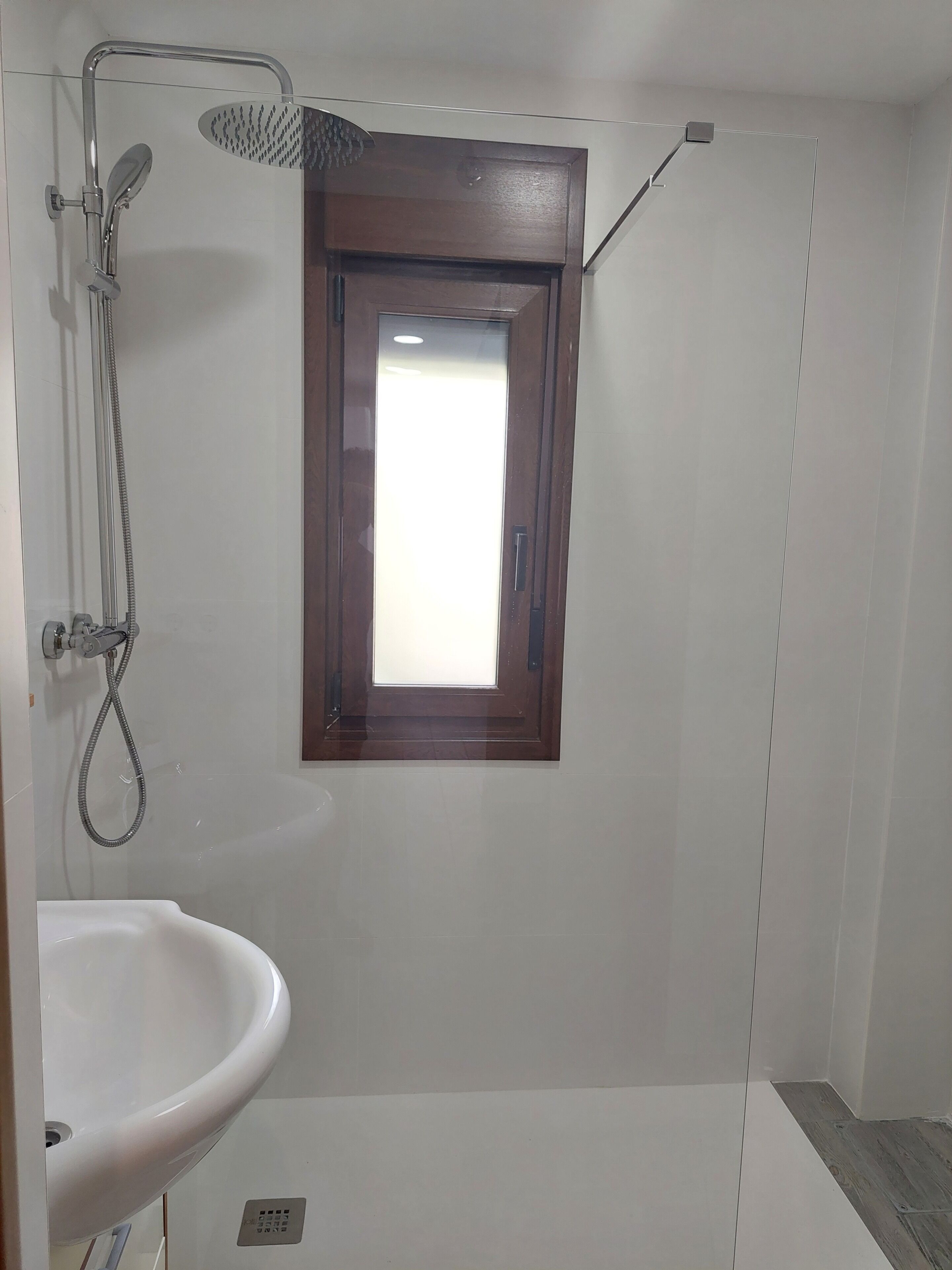 Un baño con ducha, lavamanos y una pequeña ventana.