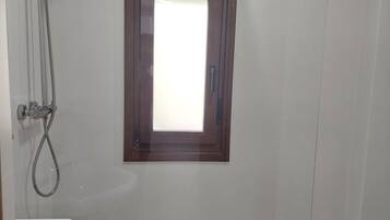 Un baño con ducha, lavamanos y una pequeña ventana.