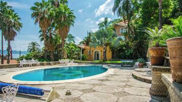 A swimming pool surrounded by palm trees and a building with a tiled roof.