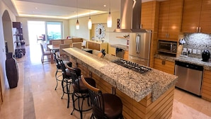 A modern kitchen with a central island, bar stools, stainless steel appliances, and wooden cabinetry.