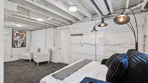 Un dormitorio con una cama, sillas a rayas, una lámpara colgante y un estante en la pared.