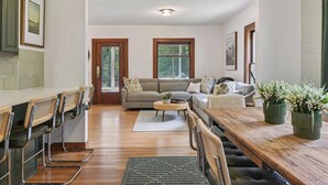 Amplia sala de estar con una mesa de comedor de madera, un sofá y una mesa de centro. Hay sillas alrededor de la mesa y una ventana con vista a zonas verdes.