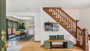 Amplia sala de estar con escalera de madera, comedor con mesa y sillas, y un cuadro grande en la pared.