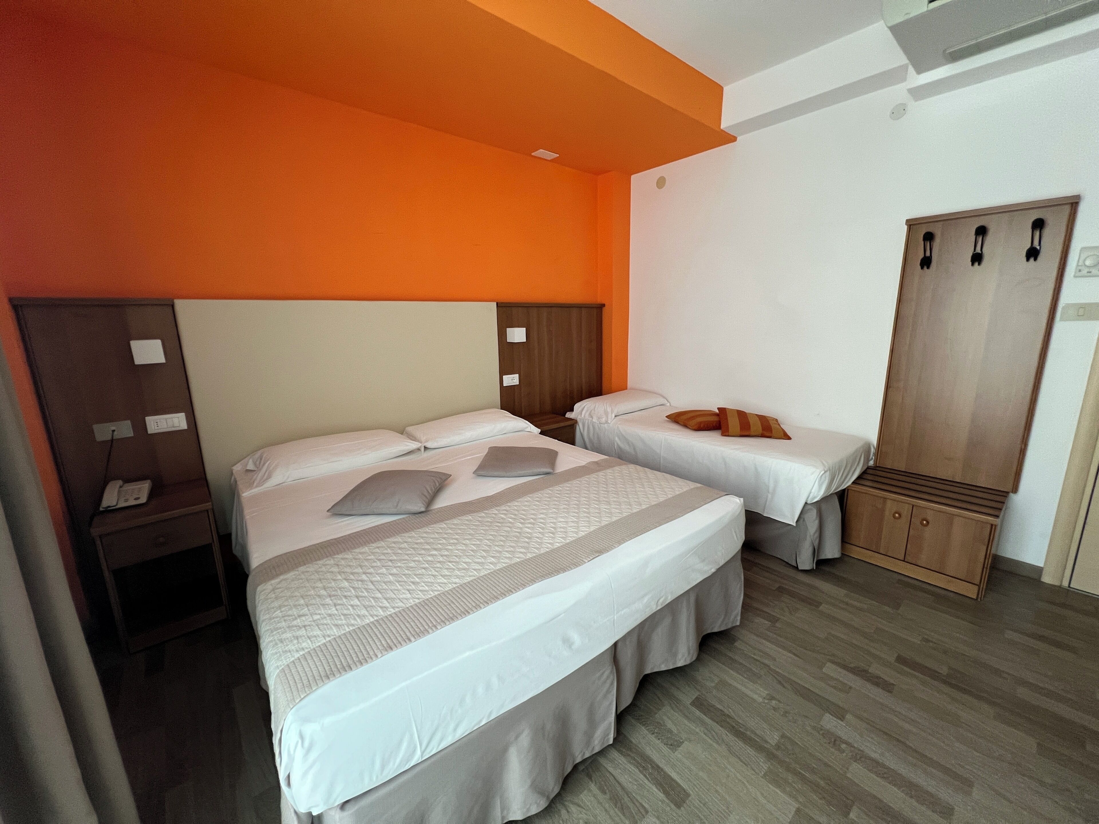 Quarto de hotel com duas camas, um guarda-roupa de madeira e uma mesa de cabeceira com telefone.