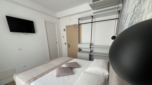 A hotel room with a bed, a flat-screen TV mounted on the wall, a door, and a window with curtains.