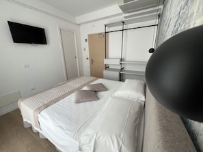 Habitación de hotel con una cama, un televisor de pantalla plana en la pared, una puerta y una ventana con cortinas.