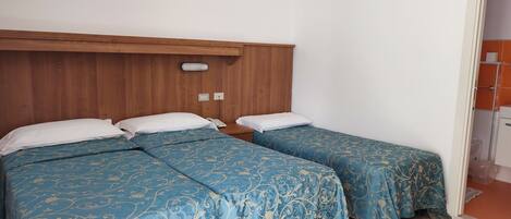 Une chambre avec deux lits, une tête de lit en bois, un téléphone sur la table de chevet et une salle de bain visible à travers une porte ouverte.