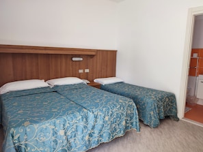 A room with two beds, a wooden headboard, a bedside telephone, and a bathroom visible through an open door. - Hotel Strand (Lido di Jesolo)