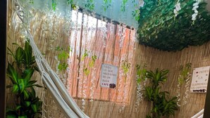 A hammock suspended between two walls with a bamboo backdrop, a potted plant, and a sign indicating the location is a cafe. - Spacious 4-Bedroom House with AC, Double Parking & Coffee Region Charm (Pereira)