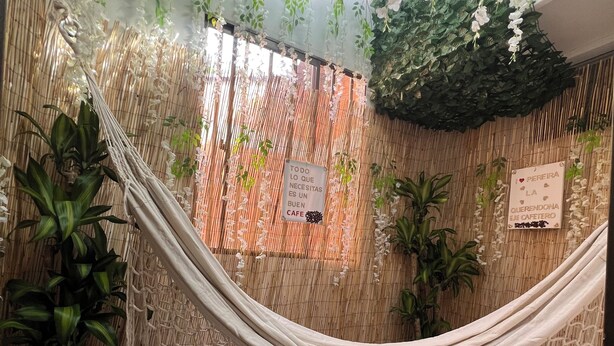 A hammock suspended between bamboo panels, with potted plants and a sign indicating a cafe. - Spacious 4-Bedroom House with AC, Double Parking & Coffee Region Charm (Pereira)