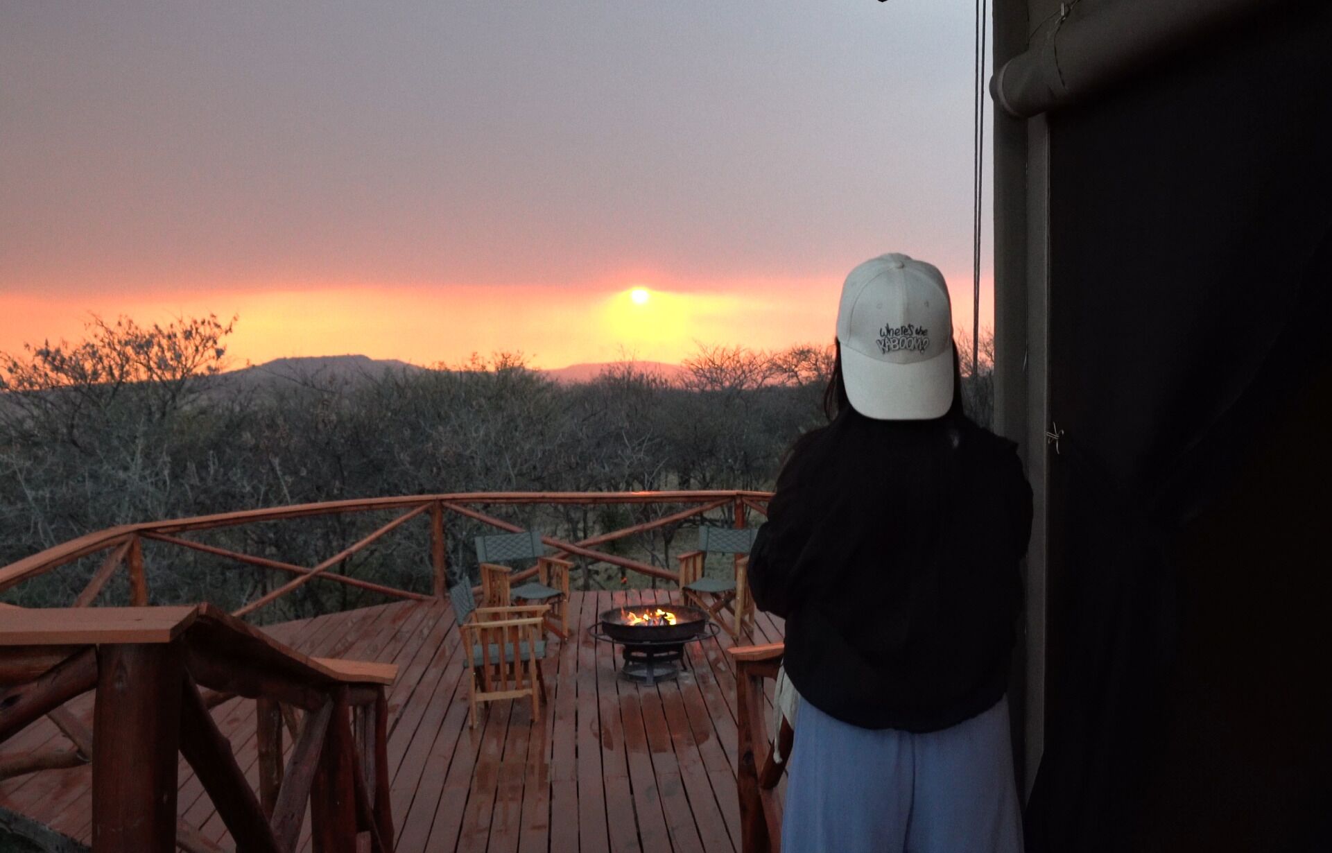 Una persona de pie sobre una cubierta de madera contemplando la puesta de sol.