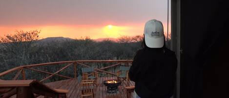 Una persona de pie sobre una cubierta de madera contemplando la puesta de sol.