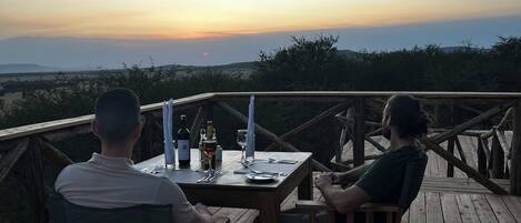 Two people seated at a wooden table on a deck with a view of the sunset.