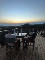 Duas pessoas sentadas numa mesa de madeira num alpendre com vista para o pôr do sol.