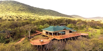 Uma cabana com telhado verde, deck de madeira e vista para uma paisagem montanhosa.