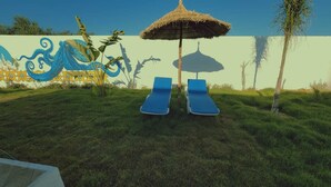A grassy outdoor area with two blue lounge chairs and a thatched umbrella. - Dar Asteroth, Villa for rent Djerba, Ghizen (Ghizen)