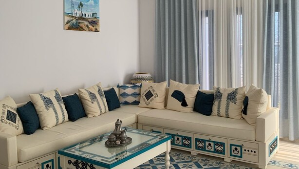 A living room with a beige sofa, patterned cushions, a glass coffee table, and a blue and white patterned floor. - Dar Asteroth, Villa for rent Djerba, Ghizen (Ghizen)