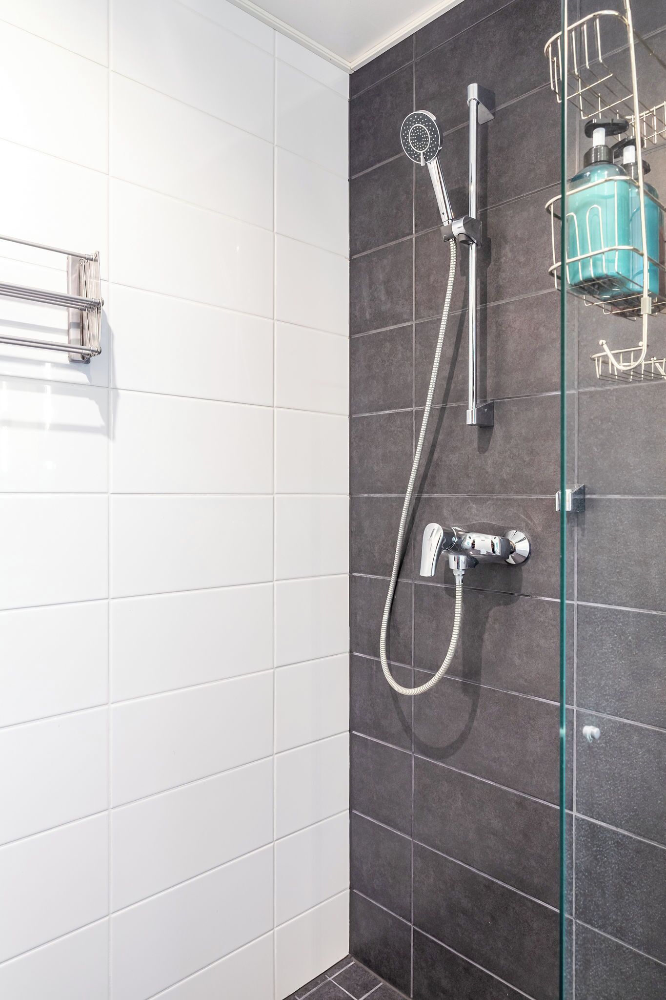 A shower with a glass enclosure, a handheld showerhead, and a wall-mounted faucet.