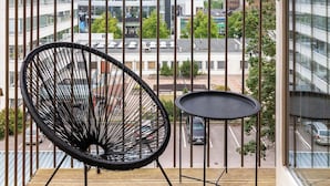 A balcony with a black chair and a small table, overlooking a cityscape with modern buildings and a parking lot. - Modern 1BR Home with Sauna & Balcony (Lahti)