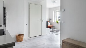 A modern kitchen with a white door, a wicker basket, and a view into a living area with a chair and a plant. - Modern 1BR Home with Sauna & Balcony (Lahti)