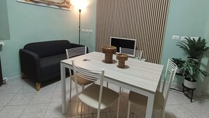 A dining area with a table and chairs, a black sofa, a painting on the wall, a clock, and a striped curtain.