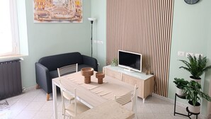 A modern living room with a sofa, a dining table, a TV, and a painting on the wall.