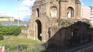An ancient stone structure with arches, surrounded by a fence and a railway track.