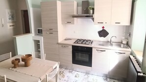 A compact kitchen with a gas stove, oven, and white cabinets. There is a dining area with a table and chairs.