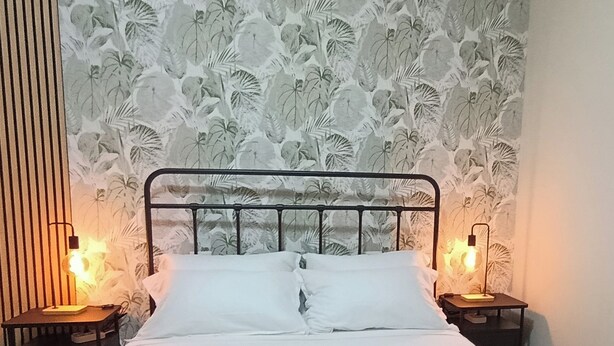 A bed with white linens, two bedside tables with lamps, a green bedspread, and a floral wallpaper background.